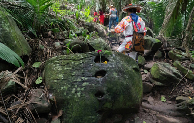 Santos Hernández Ramírez, or Maxatuxame (his name in Wixárika), dressed in a hand-embroidered shirt, guides three Wixárika families through the riverbanks of Altavista, in the municipality of Compostela, Nayarit.